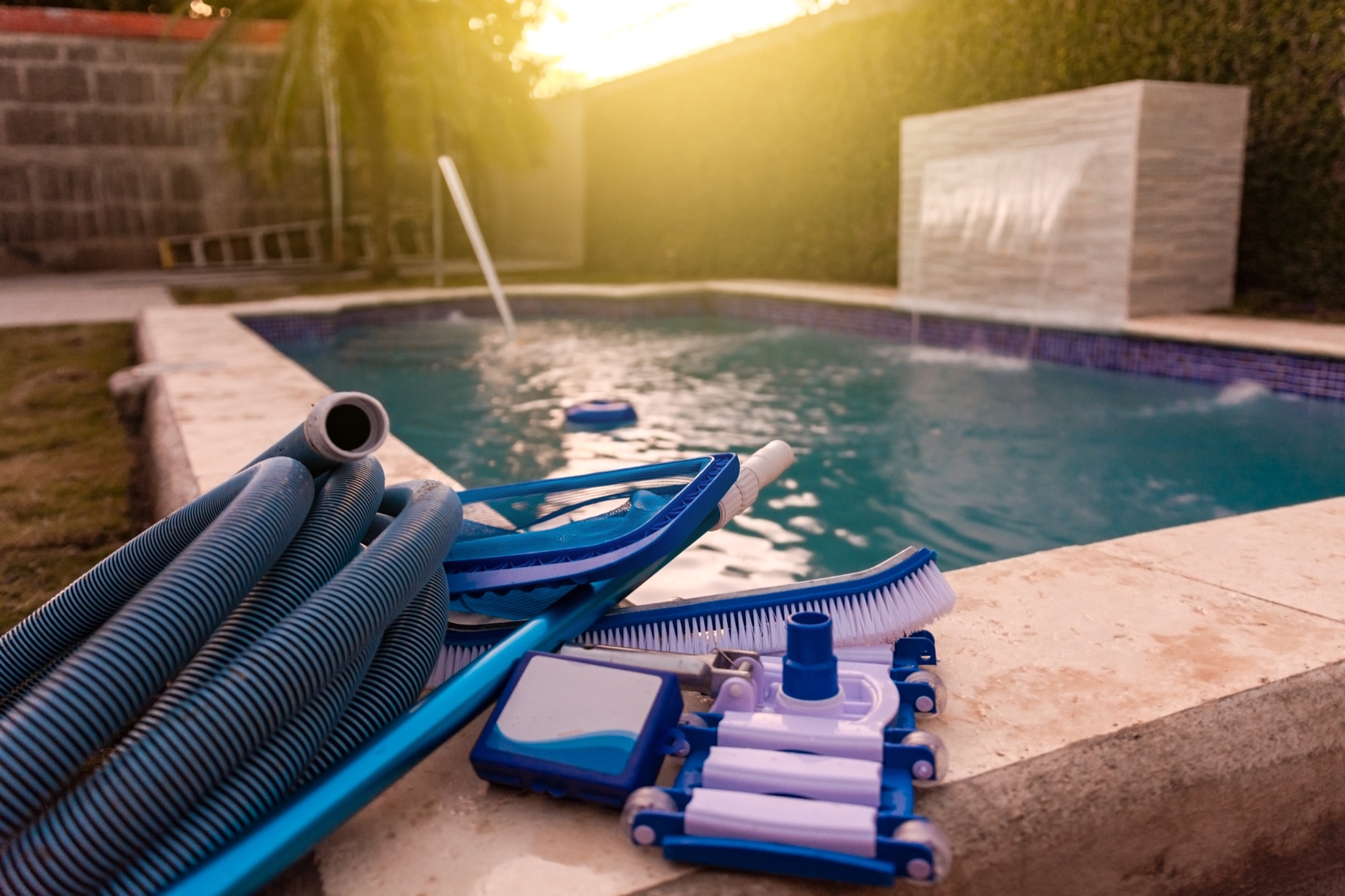 Pool maintenance equipment with brush, vacuum hose, and service tools.